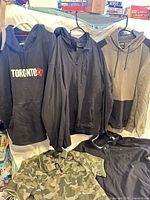 Group shot of all five tops displayed: three hoodies/jackets hanging, two polo shirts laid below