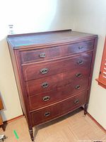 Front view of wooden dresser showing five drawers, brass pulls, turned legs