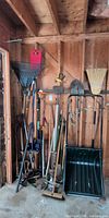 Group view of assorted long-handled yard tools in garage corner