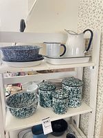 Shelf with assorted enamelware items: pitcher, measuring cup, trays, bowls, canisters, mug
