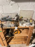 Overall lot on wooden shelf showing wire baskets with hardware, plastic organizer, drill and sander
