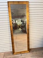 Front view of tall gold framed mirror leaning against wall