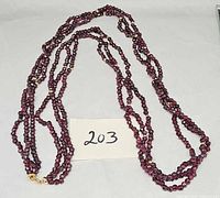 Full view of three-strand garnet bead necklace coiled, clasp visible