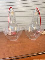 Two clear glass pendant lights with red cords displayed on tabletop