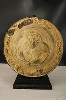 Full view of round cast metal portrait plaque on stand