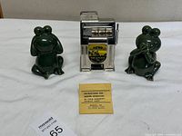 Group view of two ceramic frog banks and metal slot machine bank with instruction sheet