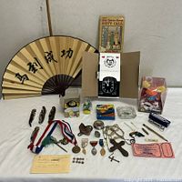 Overview shot of entire lot including fan, knives, medals, watch, boxed cards, acrylic figurine cube and assorted small items