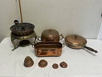 Entire lot showing chafing dish on stand, round pot, oval pan, sauté pan with lid, five molds