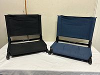 Pair of black and navy folding stadium seats side by side, seats opened and upright on table