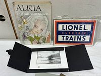 Book, Lionel sign and Kinkade print in folder displayed together