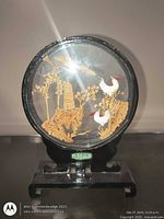 Front view of round glass cork scene, birds and pagoda visible, on wood stand