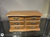 Front view of wooden jewelry box showing six drawer fronts with metal pulls