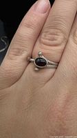 Top view of sterling silver ring worn on finger showing oval red garnet cabochon and silver bead accents