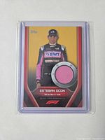Front of 2022 Topps Esteban Ocon gold relic card showing driver image and pink fabric swatch