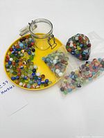 Jar, mesh bag, plastic bag and loose marbles on yellow tray