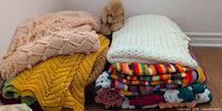 Two stacks of assorted knit and crochet blankets with Gund puppy on top