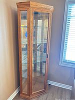 Full view of oak corner curio cabinet showing glass door, shelves, mirrored back