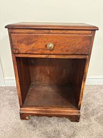 Front view of nightstand showing drawer, glass knob, open shelf, scalloped base