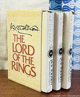 Front angled view of slipcase with three books inside, showing author signature and title