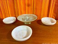 Four bowls on wood surface; three white bowls with gold spatter, one larger green footed bowl