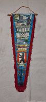 Front view of triangular Berlin anniversary pennant showing landmarks, Olympic rings, bear crest, fringe and hanging cord