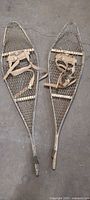 Full view of both snowshoes, showing aluminum frame, wood crossbars, webbing, canvas straps