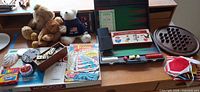 Wide shot of entire lot on desk showing Monopoly, backgammon, dominoes, comic, teddy bears, peg board game and doll clothes