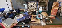 Overall lot on table showing matzah plate, menorahs, kiddush cups, challah covers, mezuzahs, books