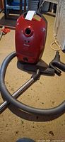 Front view of Miele red canister vacuum with hose, wand and attachments on floor