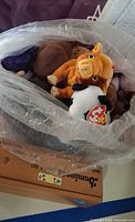 Bag containing multiple TY Beanie Babies including orange horned animal and cow, dominoes box underneath