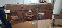 Full front view of brown textured steamer trunk with decals and hardware