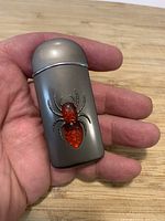 Front view of gunmetal lighter showing size and red resin spider inlay held in hand