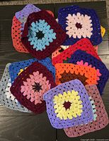Stack of fifteen multicoloured crocheted granny squares displayed on dark surface