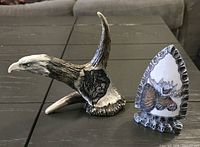 Eagle head resin sculpture with wolf relief beside triangular resin plaque with moose relief on dark table