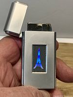 Front view of chrome lighter with lid open showing blue LED-lit Eiffel Tower design