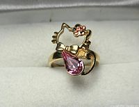 Ring front view showing cat outline, bow, pink teardrop stone, pink rhinestone flower
