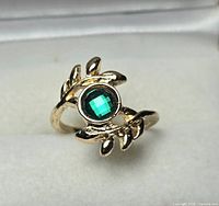 Front view of gold-tone leaf ring with green faceted stone