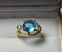 Front view showing blue center stone, gold-tone setting and clear side accents