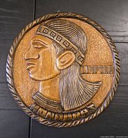 Front view of carved hardwood round plaque depicting indigenous profile and inscription