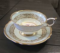 Teacup on saucer, side view showing pale green color, gold scroll border, handle