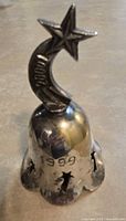 Front view of silver-plated bell showing 1999 engraving, crescent moon and star finial, star cutouts