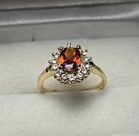 front view of ring showing oval red center stone and clear halo stones