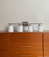 Full view of four-light brushed nickel vanity light with frosted glass shades on dresser