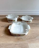 Three Corning Ware Spice of Life casserole dishes with lids shown on wooden floor