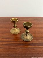 Two brass candle holders on wooden surface, front view