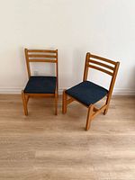 Front angled view of both Carrier wooden chairs showing blue upholstered seats and ladder backs