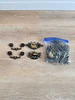 Four loose ornate metal drawer pulls and sealed bag with additional hardware