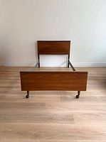 Full view of bed frame from foot showing wood veneer footboard, rails, casters, headboard