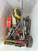 Top view of assorted tools in bin showing tape measure, sockets, screwdrivers, files, hammer head, wheel
