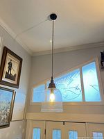 Full view of chandelier hanging from ceiling showing glass shade, wood accent, jute cord and canopy